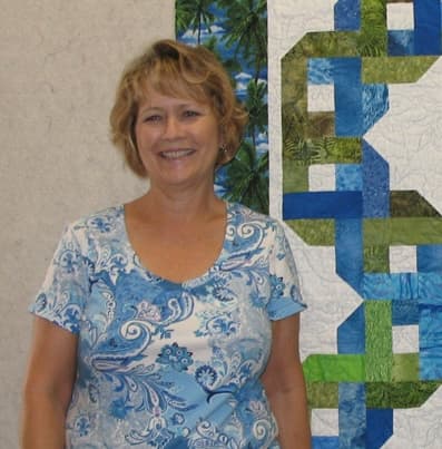 Susan K. in front of a blue and green quilt